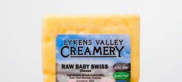 A block of Lykens Valley Creamery Raw Baby Swiss Cheese on a wooden surface.