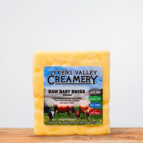 A block of Lykens Valley Creamery Raw Baby Swiss Cheese on a wooden surface.
